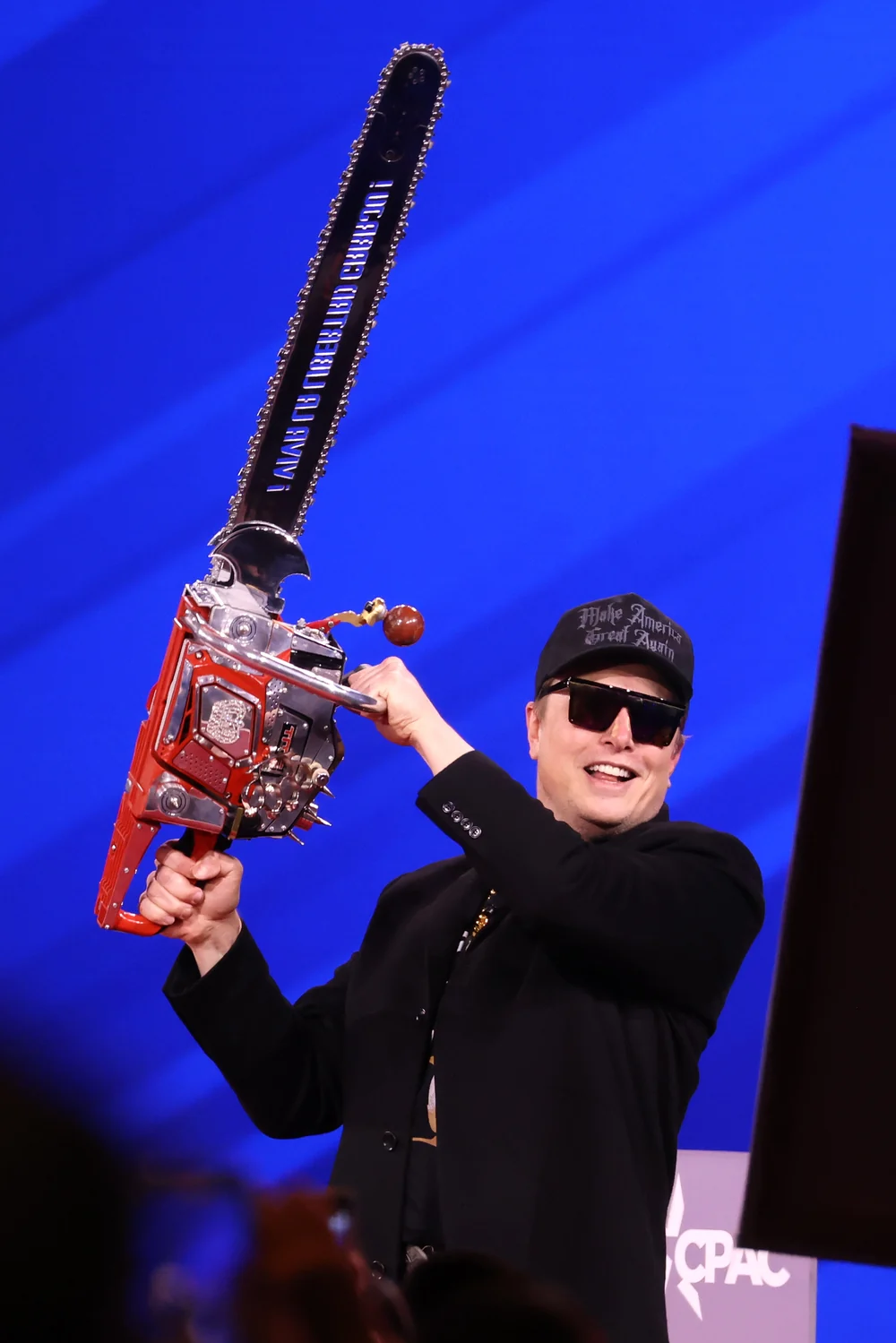 Elon Musk holding a chainsaw onstage at CPAC