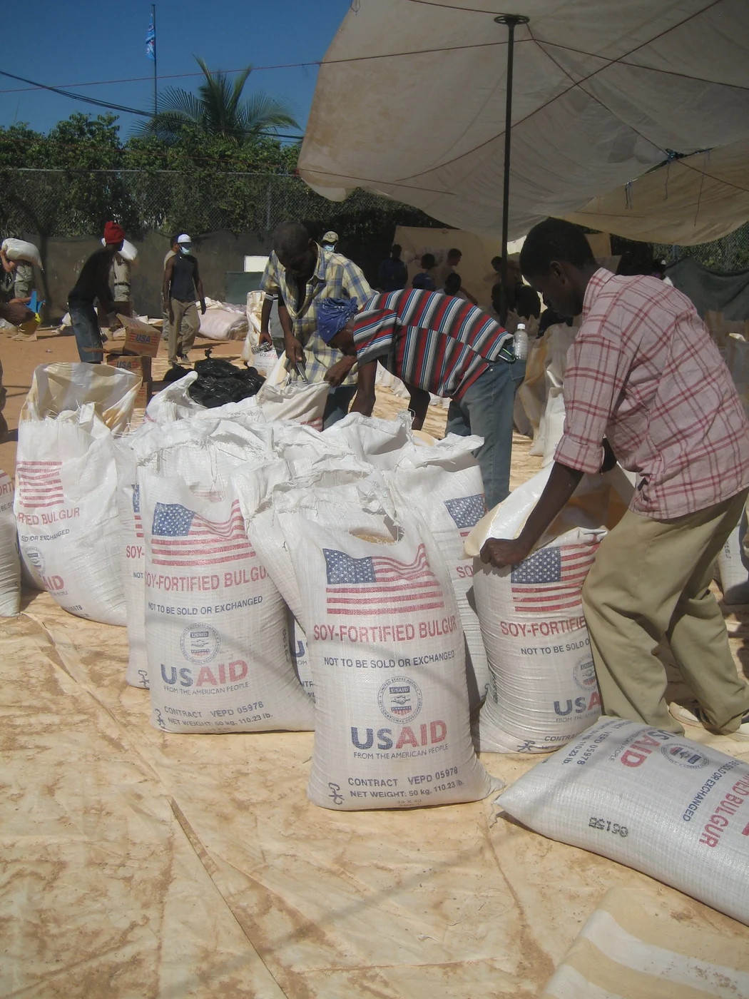Workers prepare large USAID sacks of fortified bulgur wheat at a food distribution site in Haiti