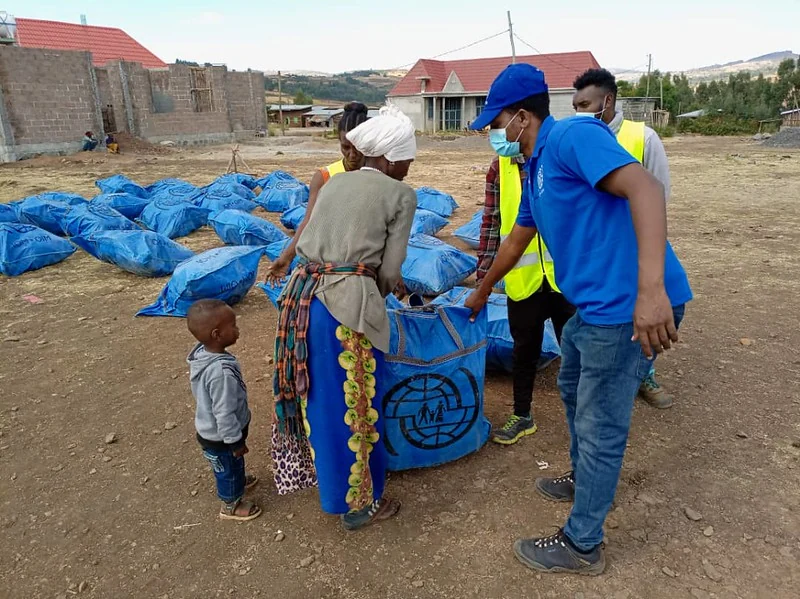 Aid workers help a woman and child collect a blue shelter kit in Tigray